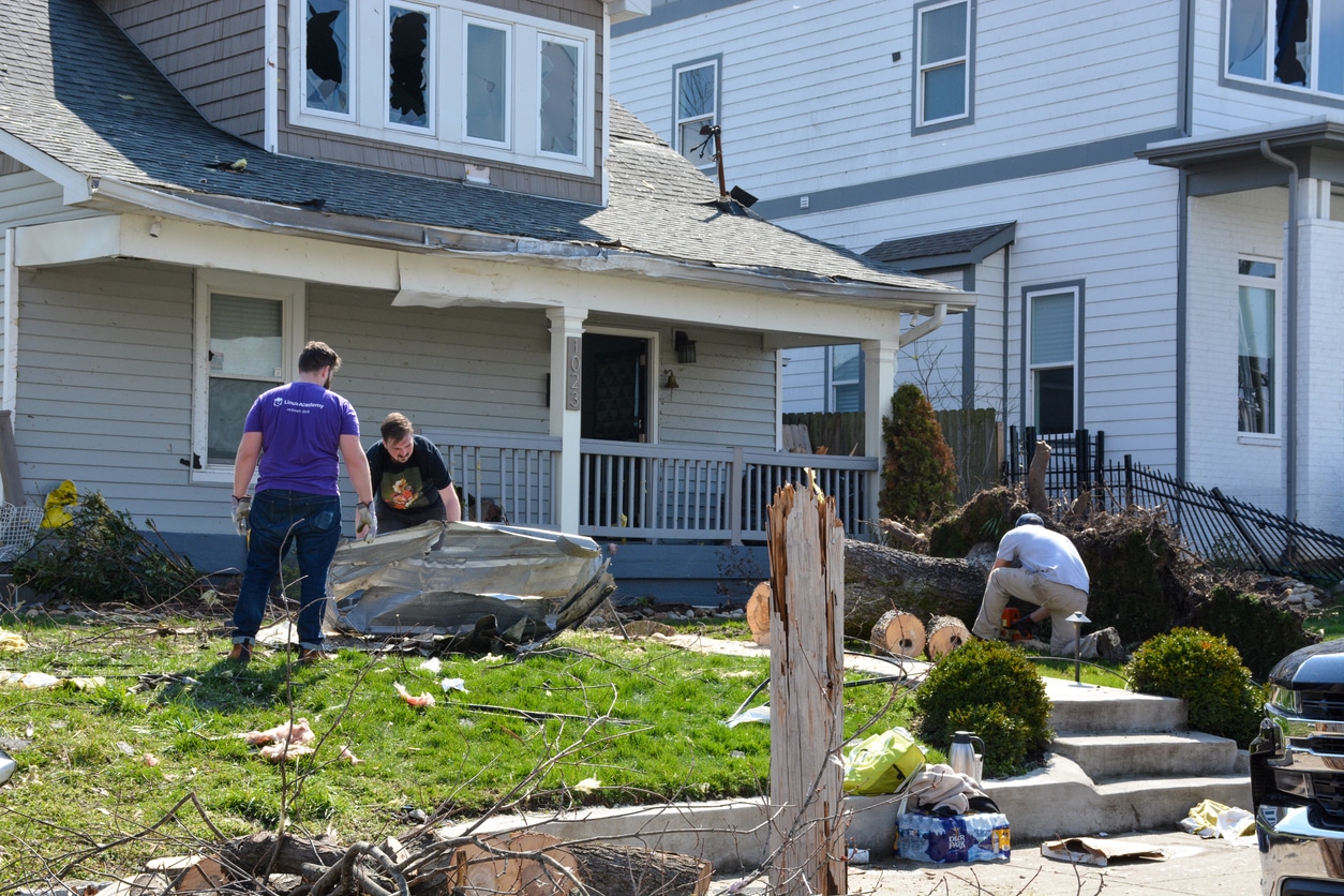 Workers clearing fallen trees and storm debris from the front yard of a wind-damaged Nashville home.