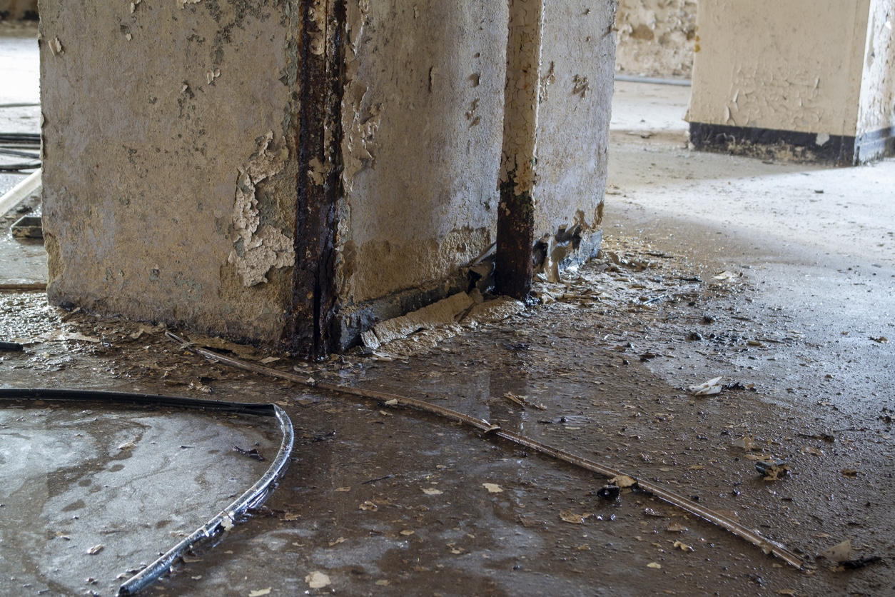 Basement flooding Nashville with peeling paint, rusted support beams, and debris scattered across a wet, deteriorating floor.